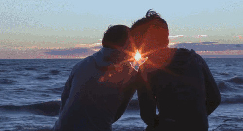 情侣坐在海边迎着夕阳亲吻gif图片