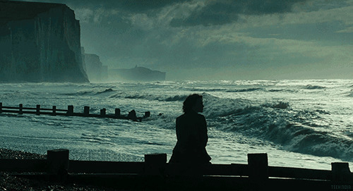 伤心的女孩坐在海边的桥墩上看海GIF动态图