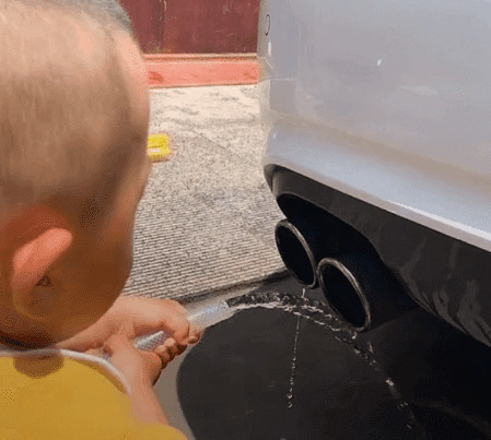 可爱的小孩子拿着水管朝汽车的尾气管冲水gif图片