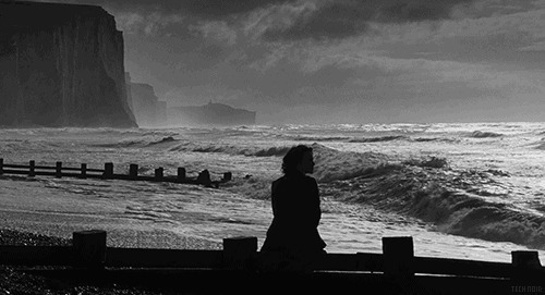 伤心的女孩坐在海边的石栏上看浪花gif图片
