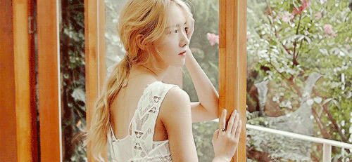 漂亮的女孩站在窗户边看着窗外盛开的花朵gif图片